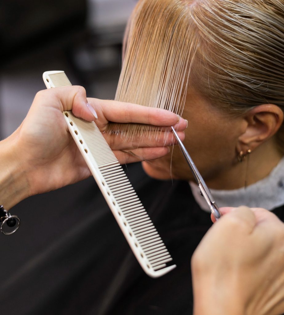 A woman getting her hair cut with scissors and comb.